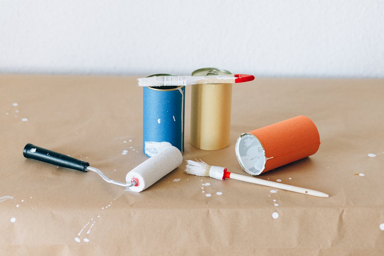 about-01 A close-up of colorful paint cans and brushes on brown paper with spilled paint creating an artistic scene.