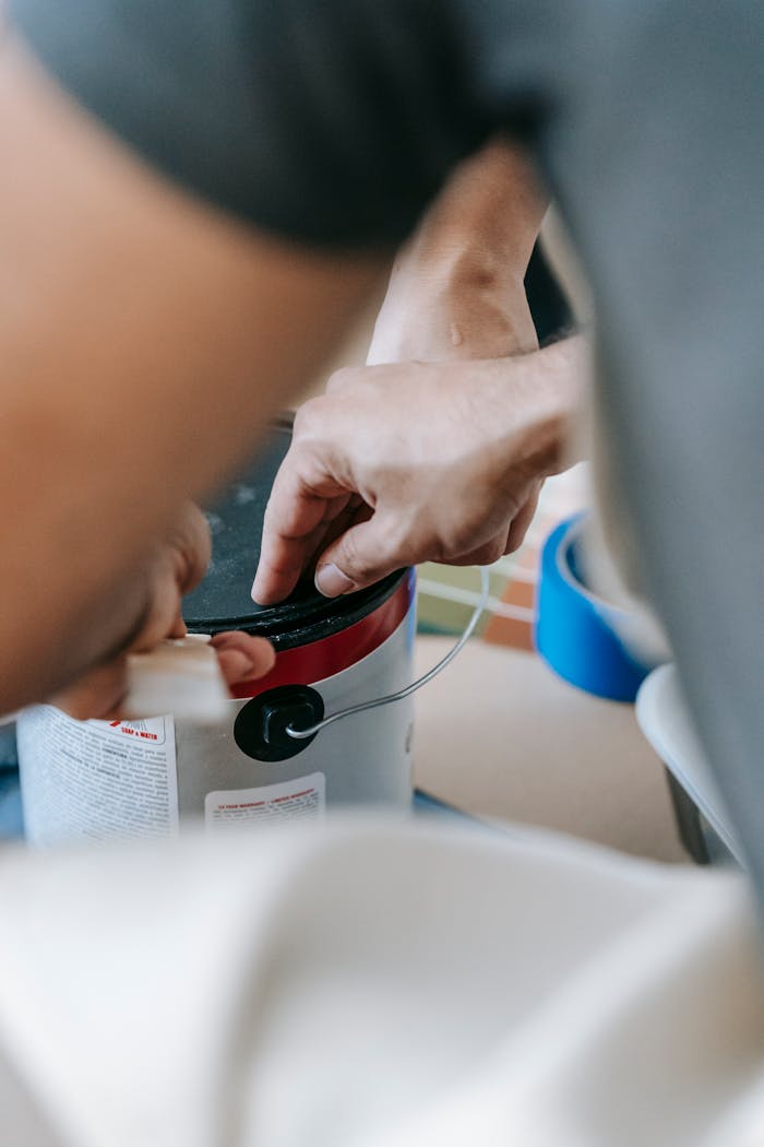 Close-up of a man opening a paint can, preparing for a home renovation with painting materials nearby.