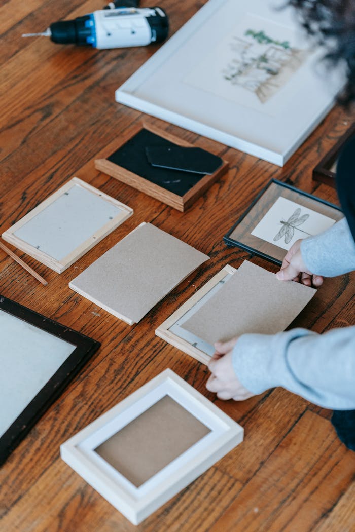 gallery-1 Person arranging picture frames on a wooden floor, preparing for home decoration.