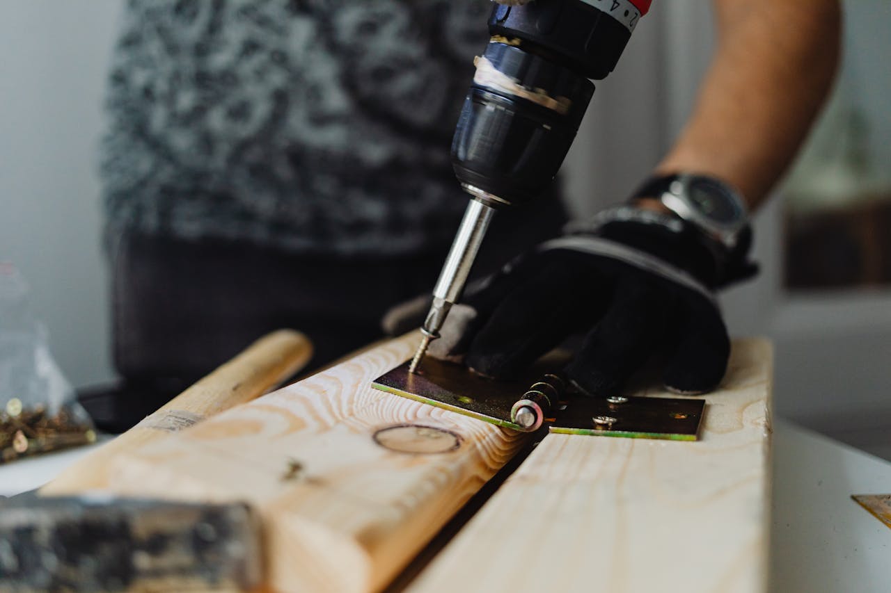 hero-img-01 Focused close-up of a handyman using a drill on a wooden plank indoors.
